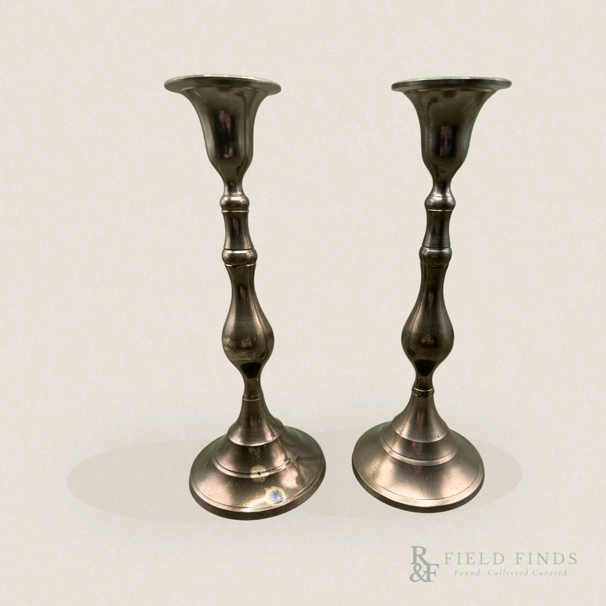 Baluster Brass Candlesticks- Pair. A pair of vintage brass candlesticks with a dark, polished metallic finish and some patina along the bass, standing side-by-side against a plain off-white background.