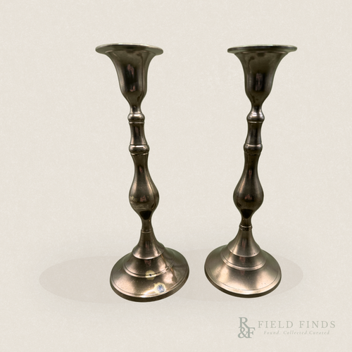 Baluster Brass Candlesticks- Pair. A pair of vintage brass candlesticks with a dark, polished metallic finish and some patina along the bass, standing side-by-side against a plain off-white background.