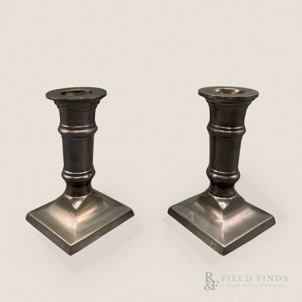 Column Candlesticks-Pair. A pair of vintage dark metal candlestick holders with square bases, shown on a light beige background with a Field Finds watermark in the lower right corner.