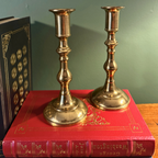 Georgian Style brass candlesticks displayed on top of a red vintage book, with a dark green wall in the background.