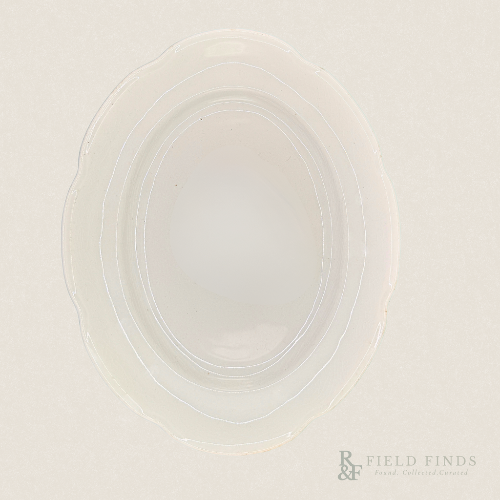 Antique White Ironstone Platter. An oval-shaped, translucent white ironstone platter with a scalloped rim, photographed from directly above on a matching off-white background. A 'Field Finds' logo is visible in the bottom right corner.