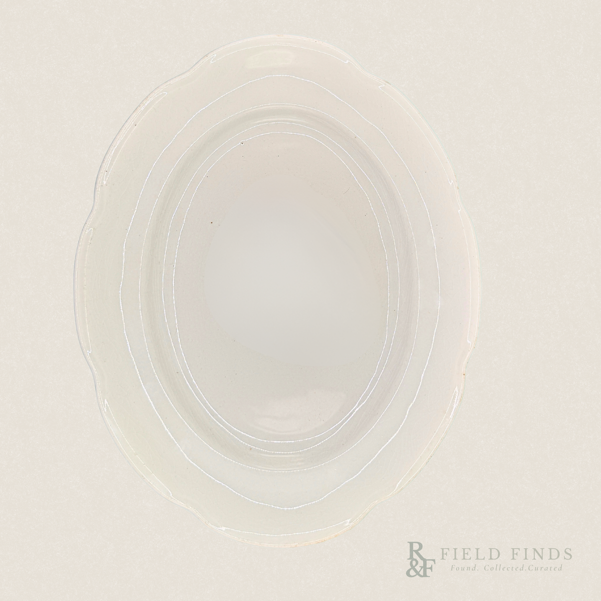 Antique White Ironstone Platter. An oval-shaped, translucent white ironstone platter with a scalloped rim, photographed from directly above on a matching off-white background. A 'Field Finds' logo is visible in the bottom right corner.